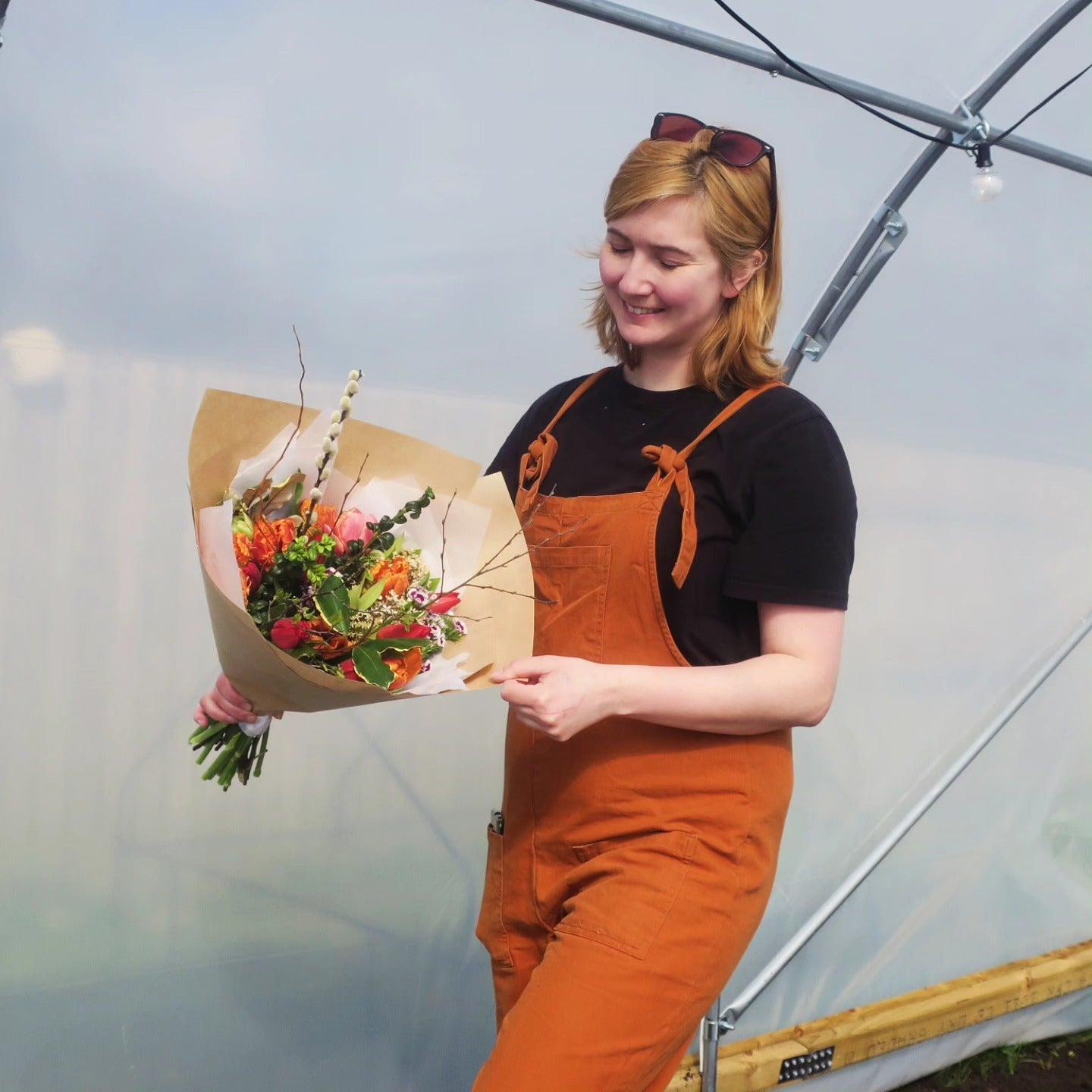 A photo of Emma Angus, founder of WilderBlooms sustainable floristry. she is wearing orange dungarees and holding a bunch of british grown flowers