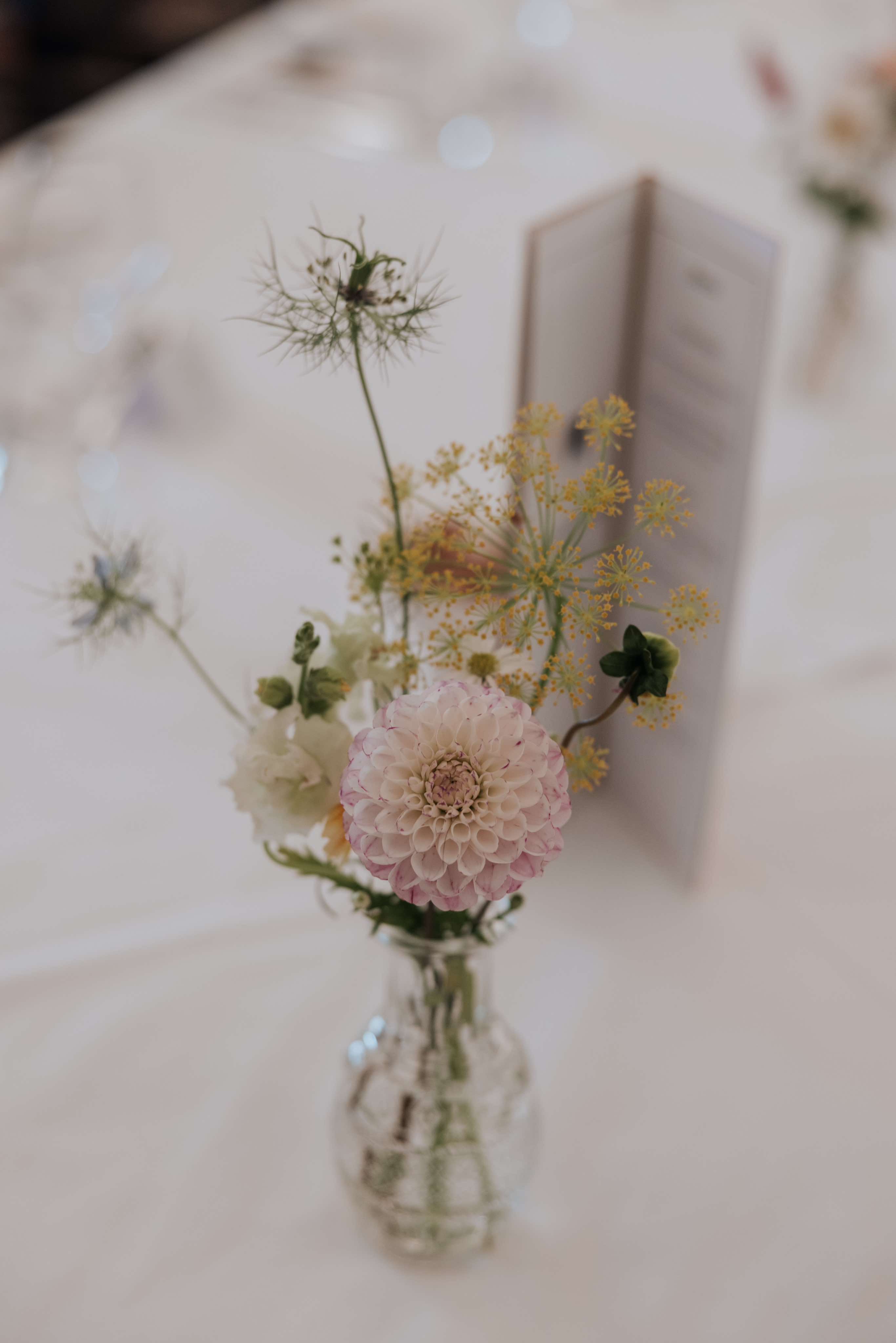 a bud vase of yellow and pink flowers sits on a table at a wedding reception